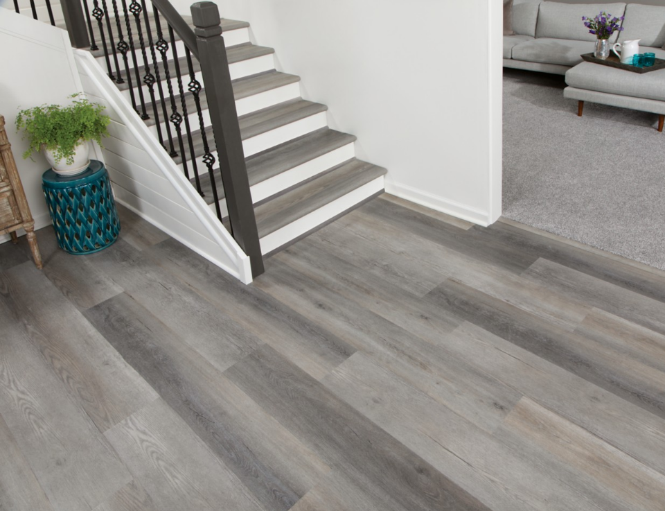 Grey wood-look flooring in an entryway and on a staircase beside a carpeted living room.