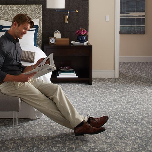 men reading on a chair in a bedroom with gray carpet floor from Johnson & Sons Flooring in Oak Ridge, TN